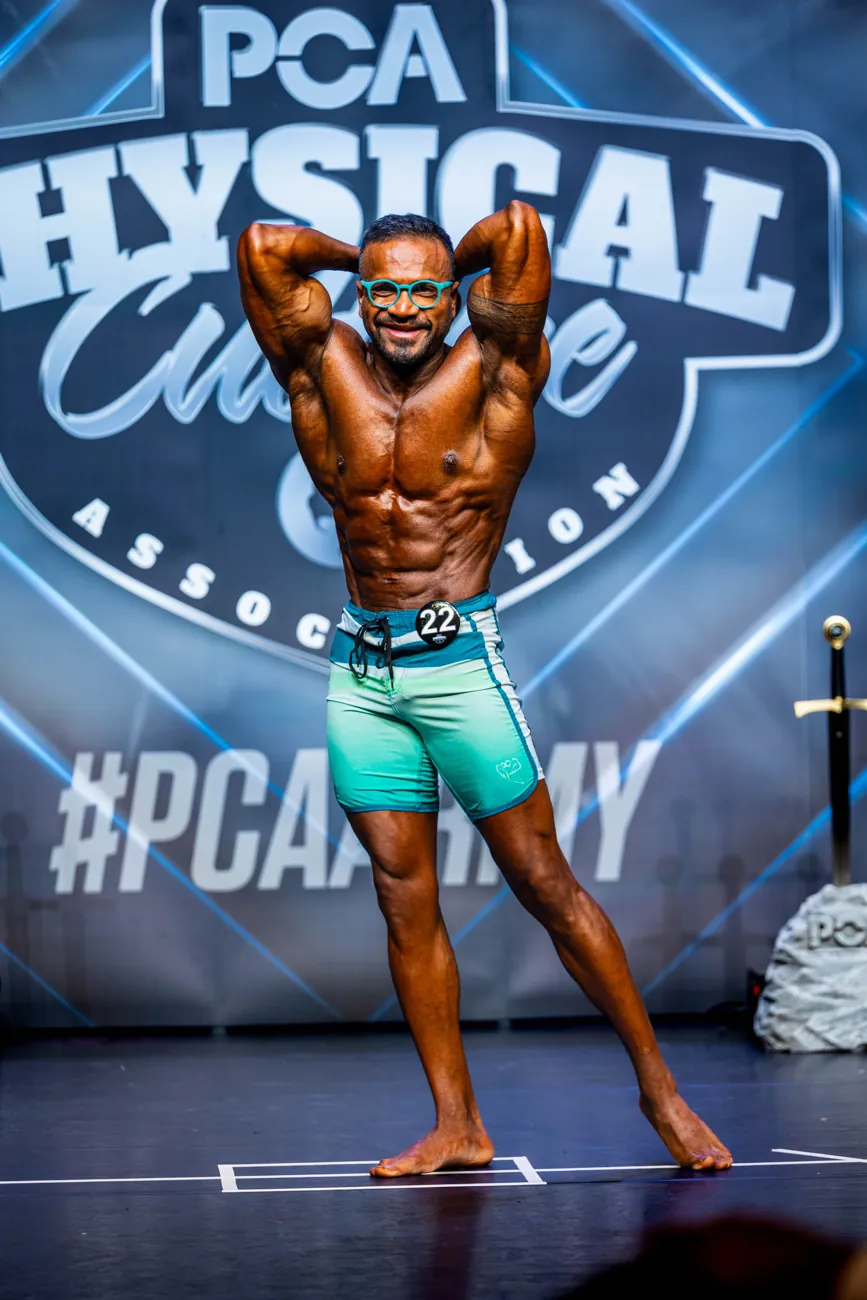Men's physique athlete with arms behind his head on stage